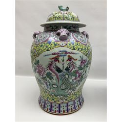 Chinese jar and cover, decorated in polychrome enamels with a panel depicting birds amongst peonies, surrounded by floral and foliate decoration on a yellow ground, with four pink mask handles and dog finial to cover, with retail sticker beneath for Wing Tung Hing, together with a similar blue and white example, decorated with figural scenes amongst trees and flowers, the cover with a temple dog finial, with printed mark beneath, tallest H41cm