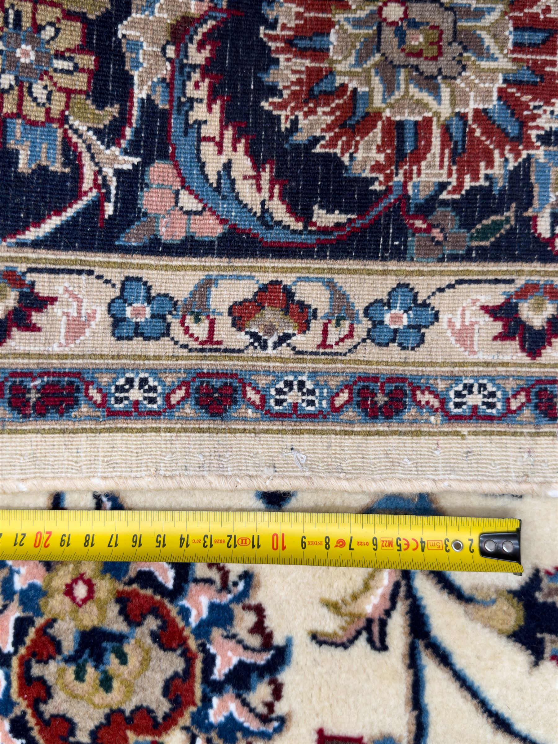 Northeastern Persian Meshed hand-knotted rug, ivory ground with an overall design of scrolling vines, palmettes, and rosettes in an indigo palette, soft blues, and madder, framed by a deep indigo border of lotus palmettes and flowerheads between multiple guard borders, 300cm x 202cm