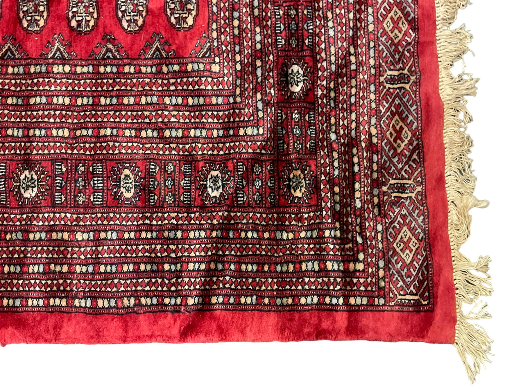 Persian Bokhara crimson ground carpet, the field decorated with repeating Gul motifs and lozenges, the multi-band geometric border with stylised plant motifs, two additional bands at the ends with geometric lozenges