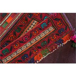 North East Persian Turkoman saddle bag, traditional double pouch form, each panel with madder red ground, decorated with horizontal bands of stylized geometric floral motifs and angular vine work, framed simple borders, central panel woven in flatweave with polychromed chequered design flanked by braided carrying cords with tasselled and knotted decorative elements 