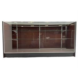 Shop display cabinet counter, glazed front and top, with mahogany laminate sides and back, enclosing two long adjustable shelves, fitted with two sliding cupboard doors to the rear, on castors