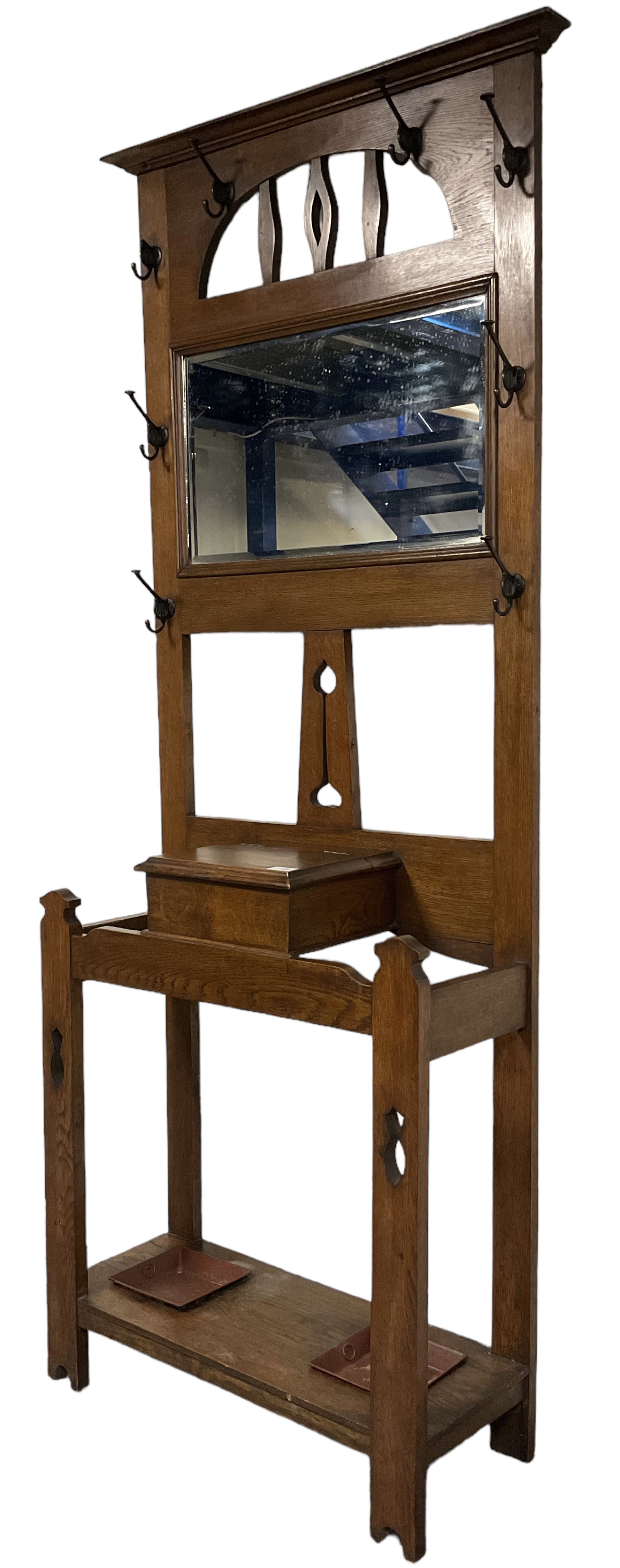 Arts & Crafts period oak hall stand, projecting moulded cornice over arched cut-out decorated with shaped vertical rails, fitted with rectangular bevelled mirror back over hinged glove compartment, on straight pierced supports with shaped pediments 