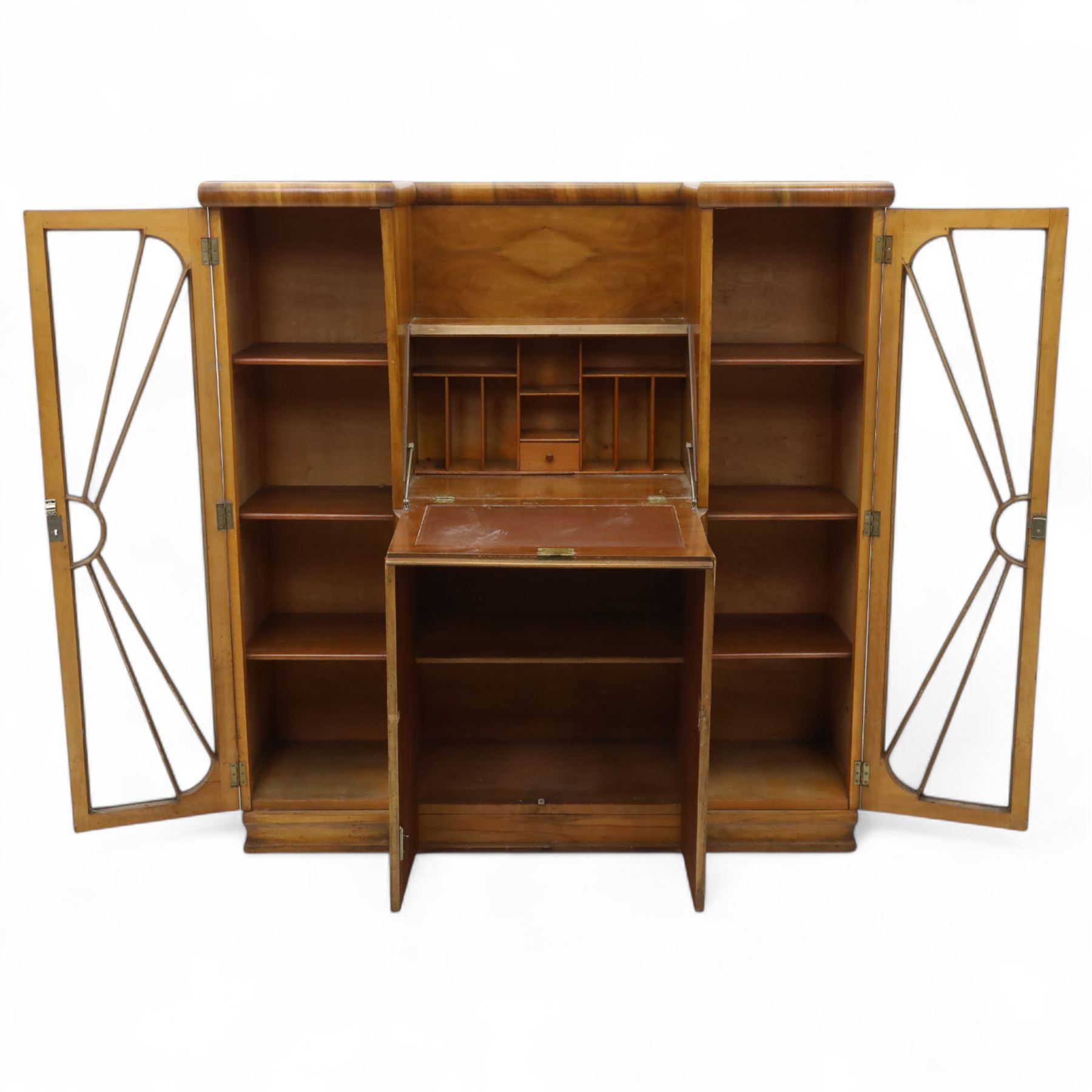 Art Deco walnut bureau bookcase, top with moulded and rounded edges and stepped front profile, central shelf, and fall-front bureau section with vertical and horizontal pigeon holes and a small drawer, above two cupboard doors and flanked by two tall glazed display cabinets with single doors and geometric sunburst design astragal glazing bars enclosing three shelves, raised on cavetto shaped plinth base 