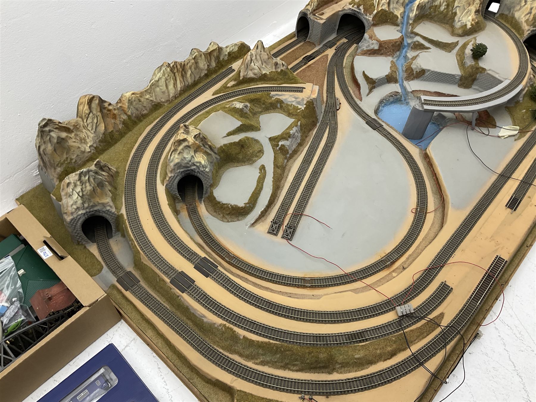 '00' gauge - table-top moulded plastic model railway layout with various rocky outcrops, tunnels, waterfall to lake, loops of Fleischmann track supplemented by Hornby track, bridges, kit built buildings and other accessories; together with Bachmann Class 150 2-car DMU Set and Hornby Northern Rail Class 142 2-car Set; both boxed; and small quantity of other rolling stock, three controllers etc  200 x 120cm