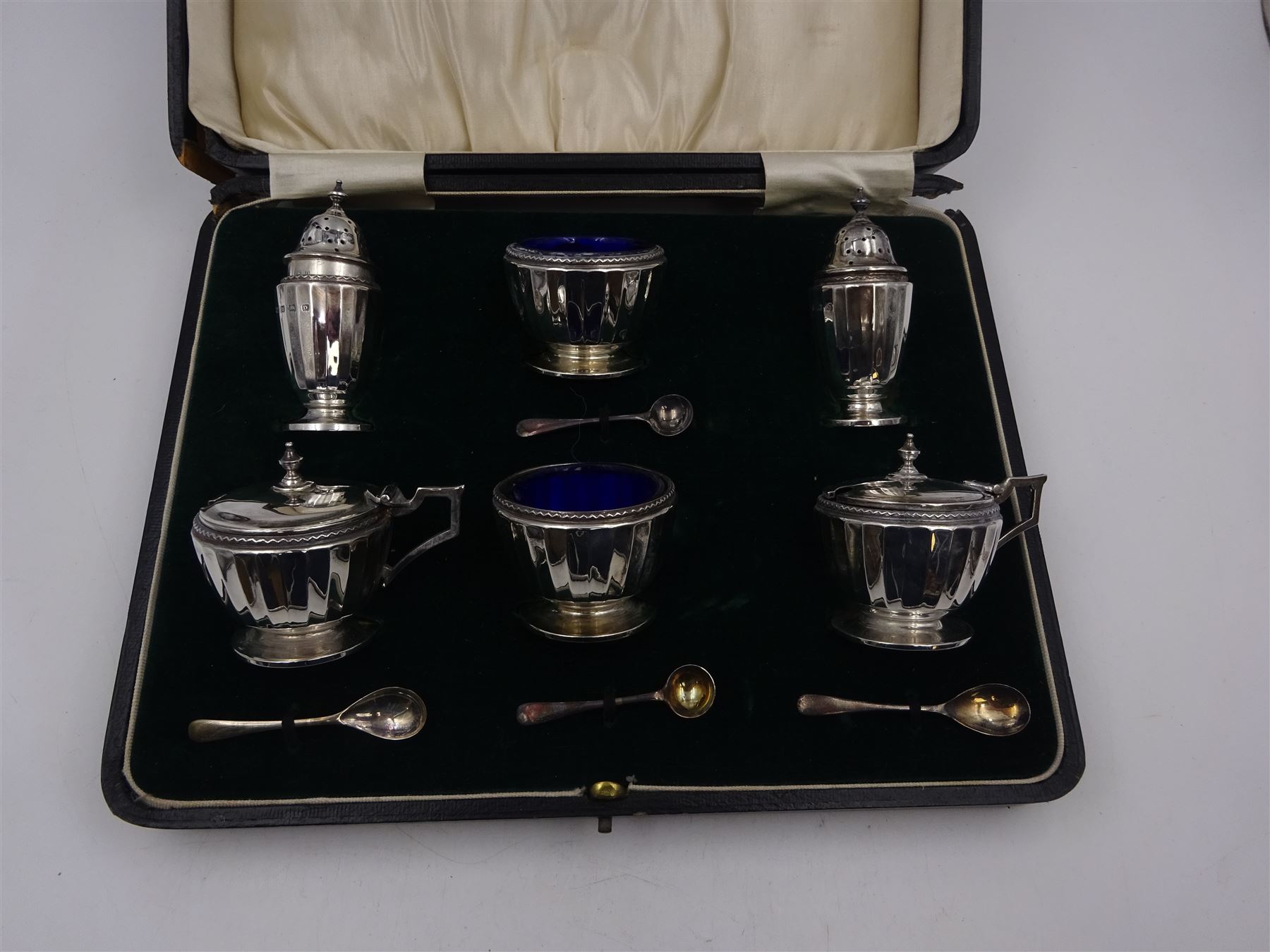 1920s silver six piece cruet set, comprising two mustard pots with covers, two open salts and two pepper pots, all of circular faceted form, mustards and salts with blue glass liners, hallmarked Mappin & Webb, Birmingham 1928, with four matched silver condiment spoons, hallmarked, contained within fitted case 