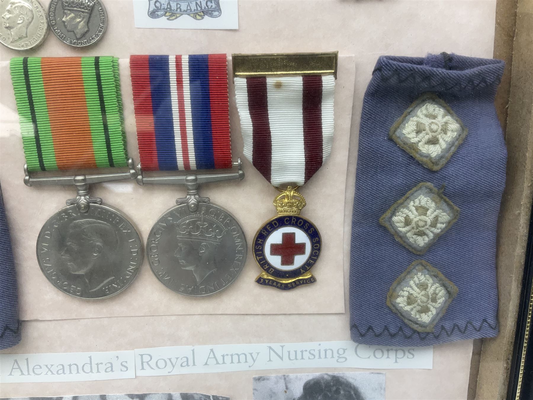Framed display of medals and badges relating to Captain Cynthia Page of Queen Alexandra's Royal Army Nursing Corps including WW2 War Medal and Defence Medal with miniatures; Red Cross Society 3-Year Service Medal; Q.A.R.A.N.C. cap badge; Girl Guide and silver Scout badges; rank epaulettes; and related photographs 33 x 23cm
