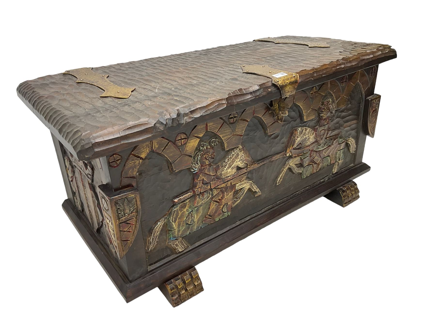 Carved wooden blanket chest, the tooled hinged lid with shaped metal strap hinges and catch, the front carved with arcade over two medieval jousters, on carved sledge feet