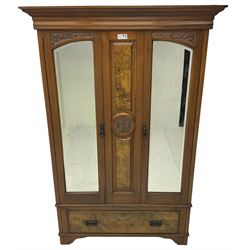 Edwardian walnut double wardrobe, enclosed by two bevelled mirror doors flanking central figured panel with foliate carved decoration, fitted with single drawer to base