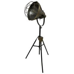 Industrial tripod spotlight, with a metal shade and wire guard, supported by a height-adjustable tripod base, the head equipped with an adjustable tilt mechanism