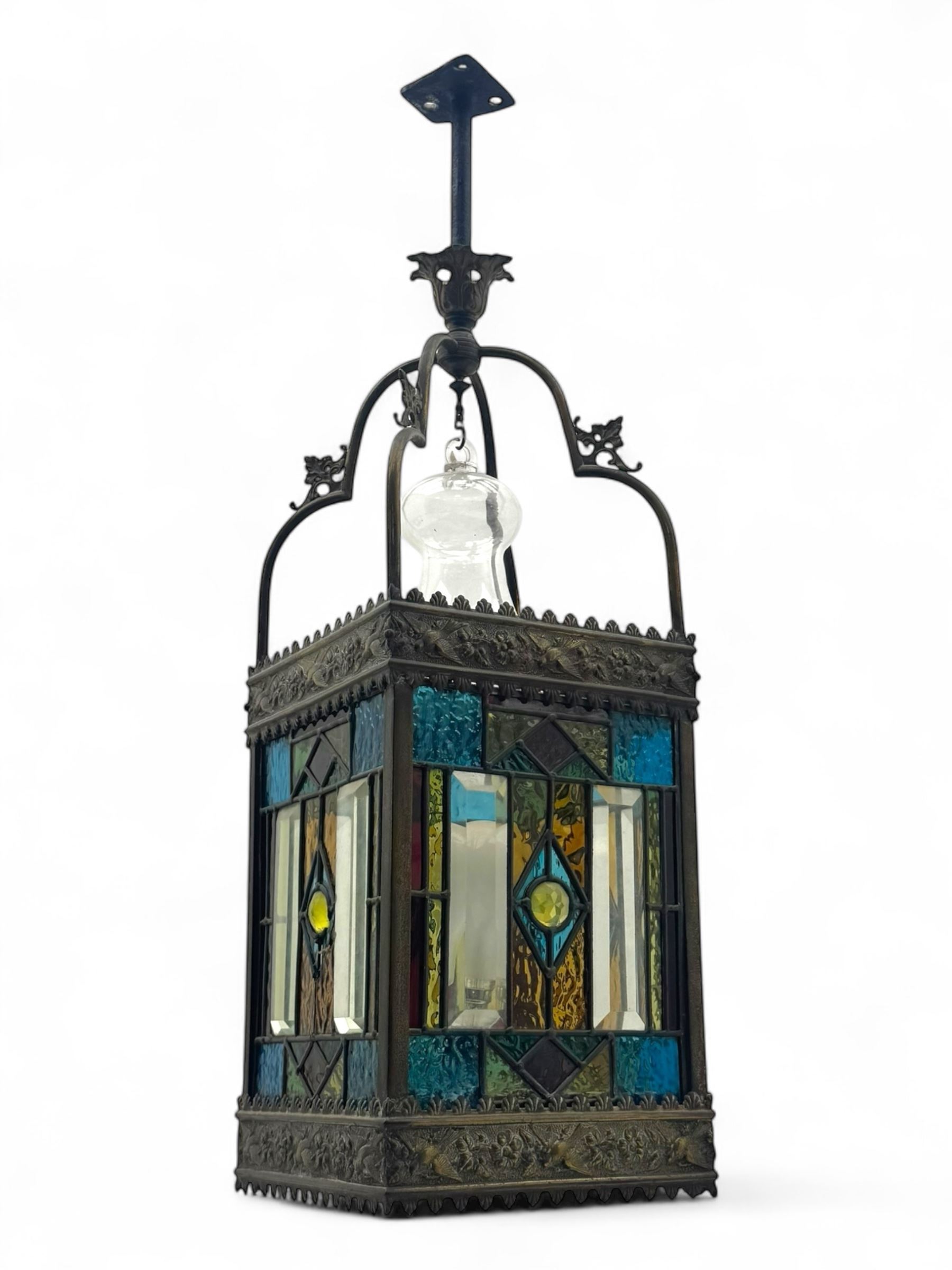 20th century Gothic design stained glass and brass hall lantern, with ornately decorated frieze and apron, with geometric coloured glass panels and eight rectangular bevelled glass panels, with bell shade, wired for electricity 