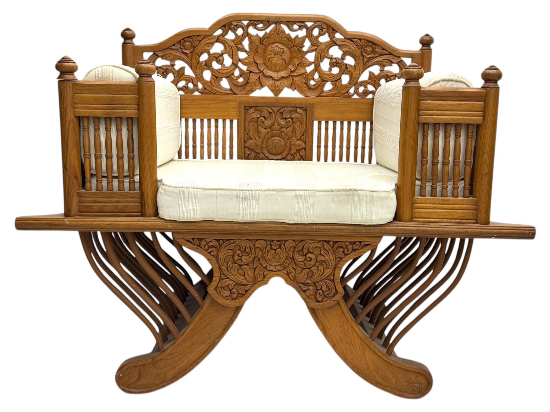 Early 20th century carved teak Howdah elephant chair, with pierced floral and foliate carved backrest, spindle gallery arm supports, cream upholstered cushions, splayed legs on a curved reeded base 