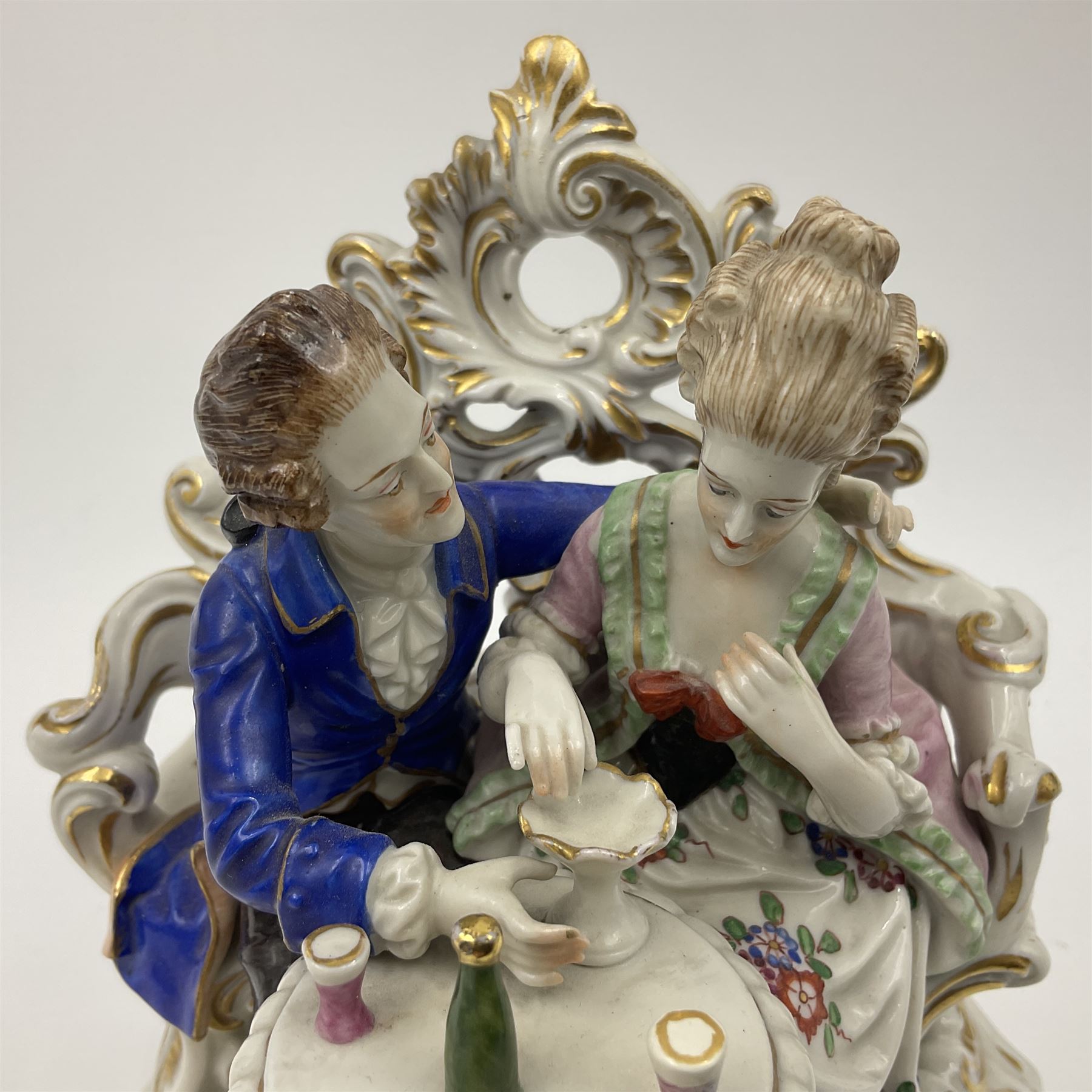 Figure group, probably Volkstedt, modelled as a courting couple seated before a table, the ornate bench and table conforming with and leading from the gilt heightened scrolling base, with blue painted mark beneath, H14.5cm
