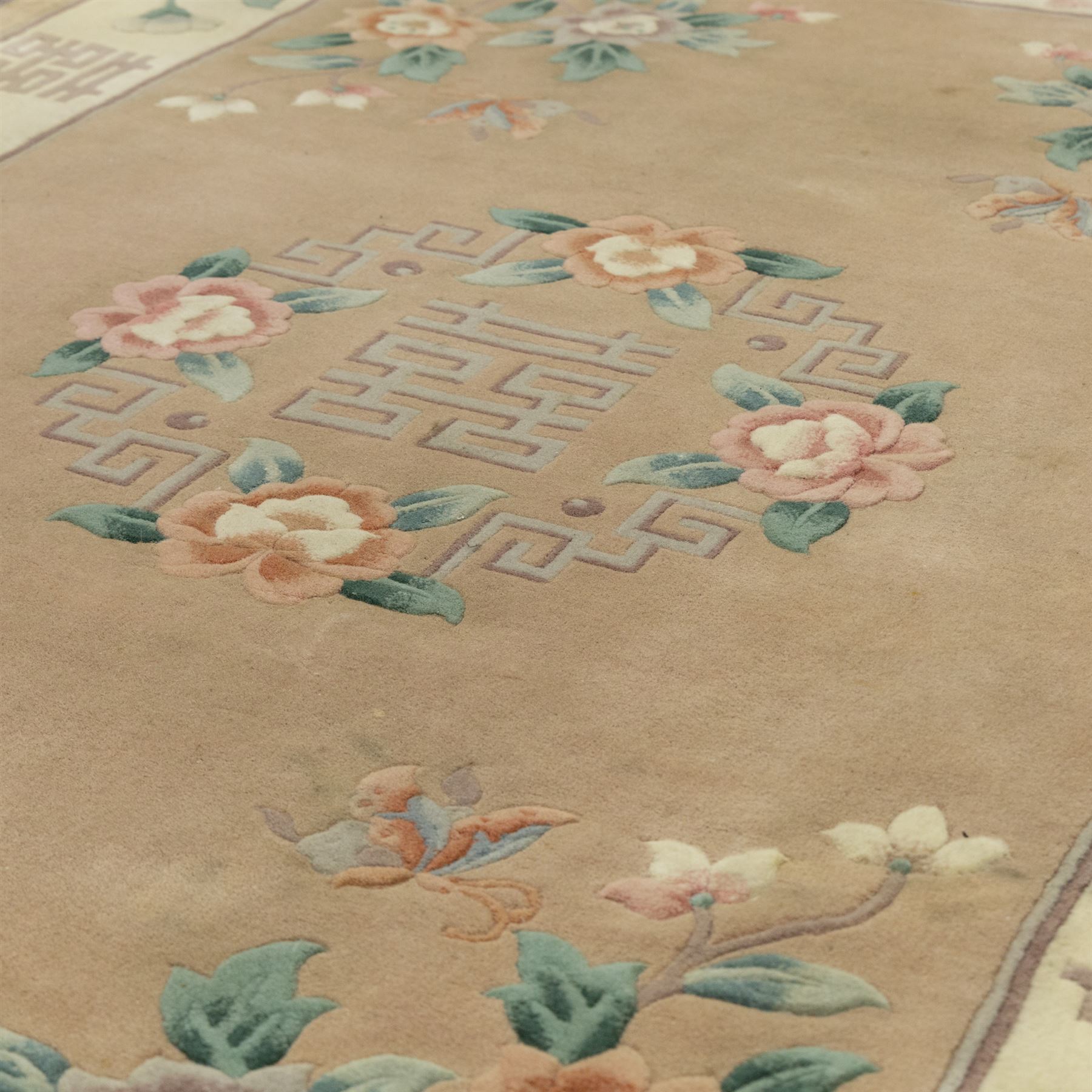 Chinese wool rug, beige ground decorated with peonies, flowering branches and butterflies, centred by a shou symbol within key pattern surround, cream border with floral sprays and double happiness motifs, cotton fringe ends