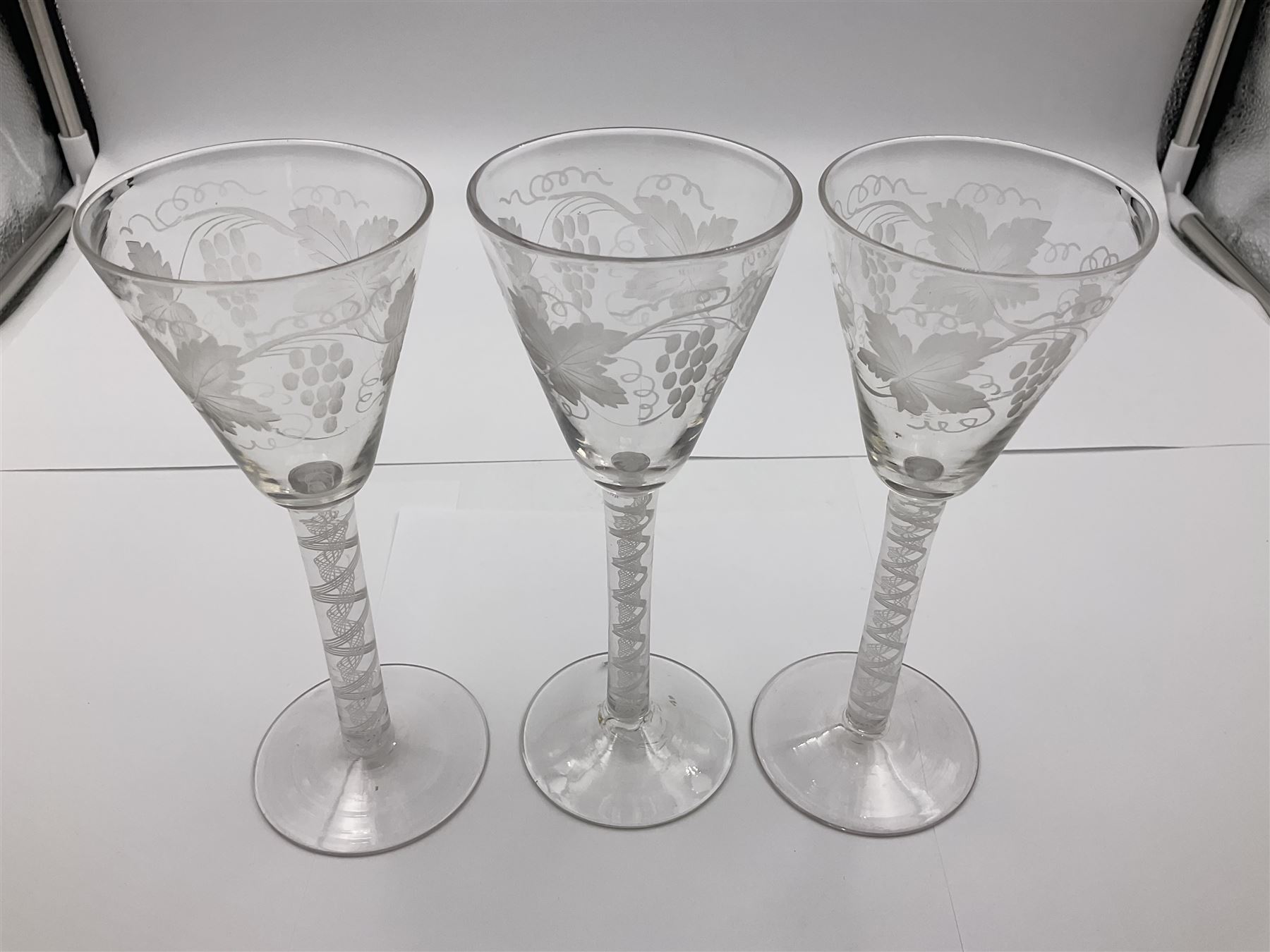Set of three 18th century style wine glasses, each with funnel bowl etched with fruit vine, upon a double series air twist stem and circular foot, H17cm