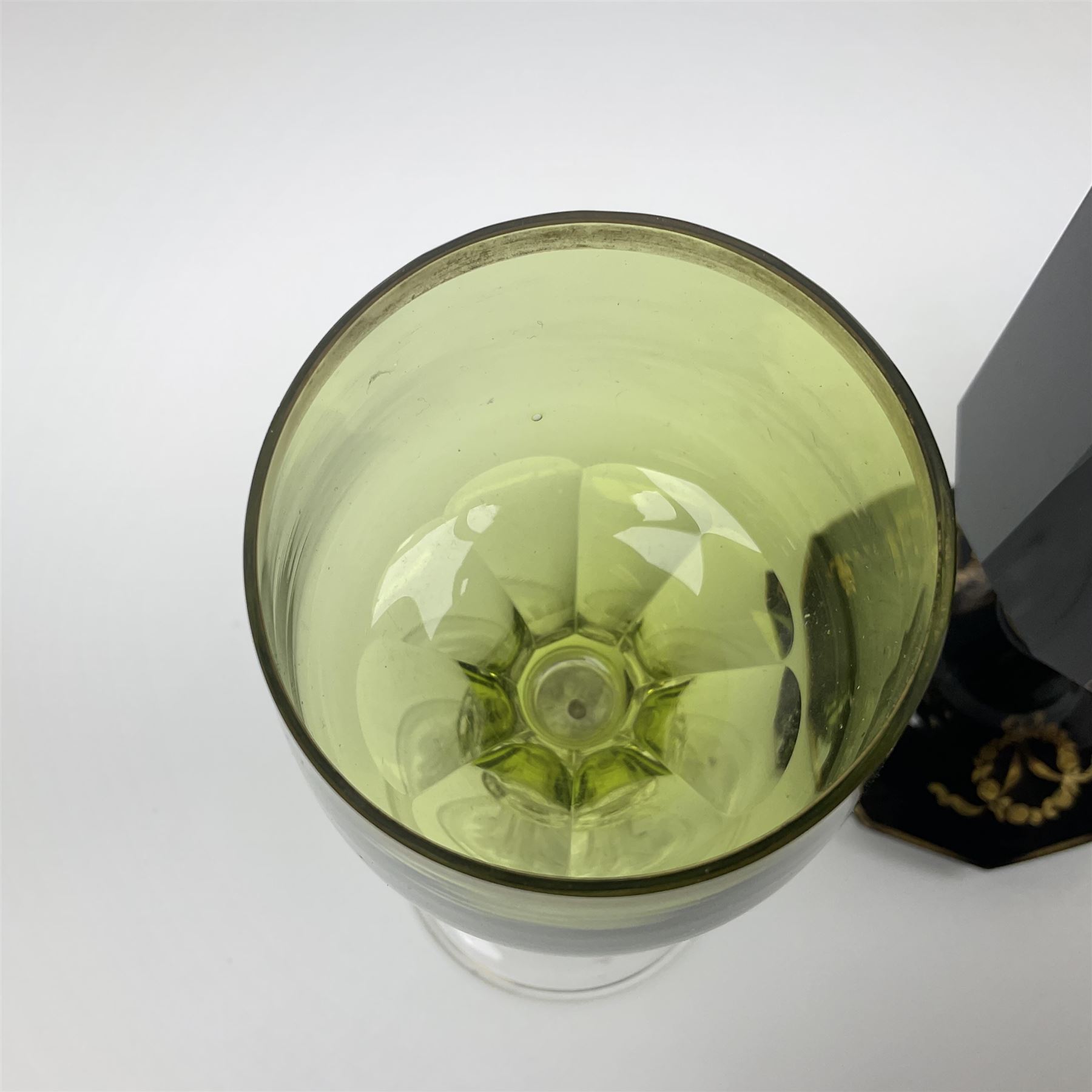 19th Century Bohemian amethyst glass lidded goblet, the bowl of faceted form, gilded with three children in period dress playing games, upon a knopped stem and conforming faceted foot, together with an art nouveau green glass goblet, with gilded rim, upon clear trumpet stem, and a hand blown wine glass, transfer printed with birds and three figures in period dress, tallest H29cm