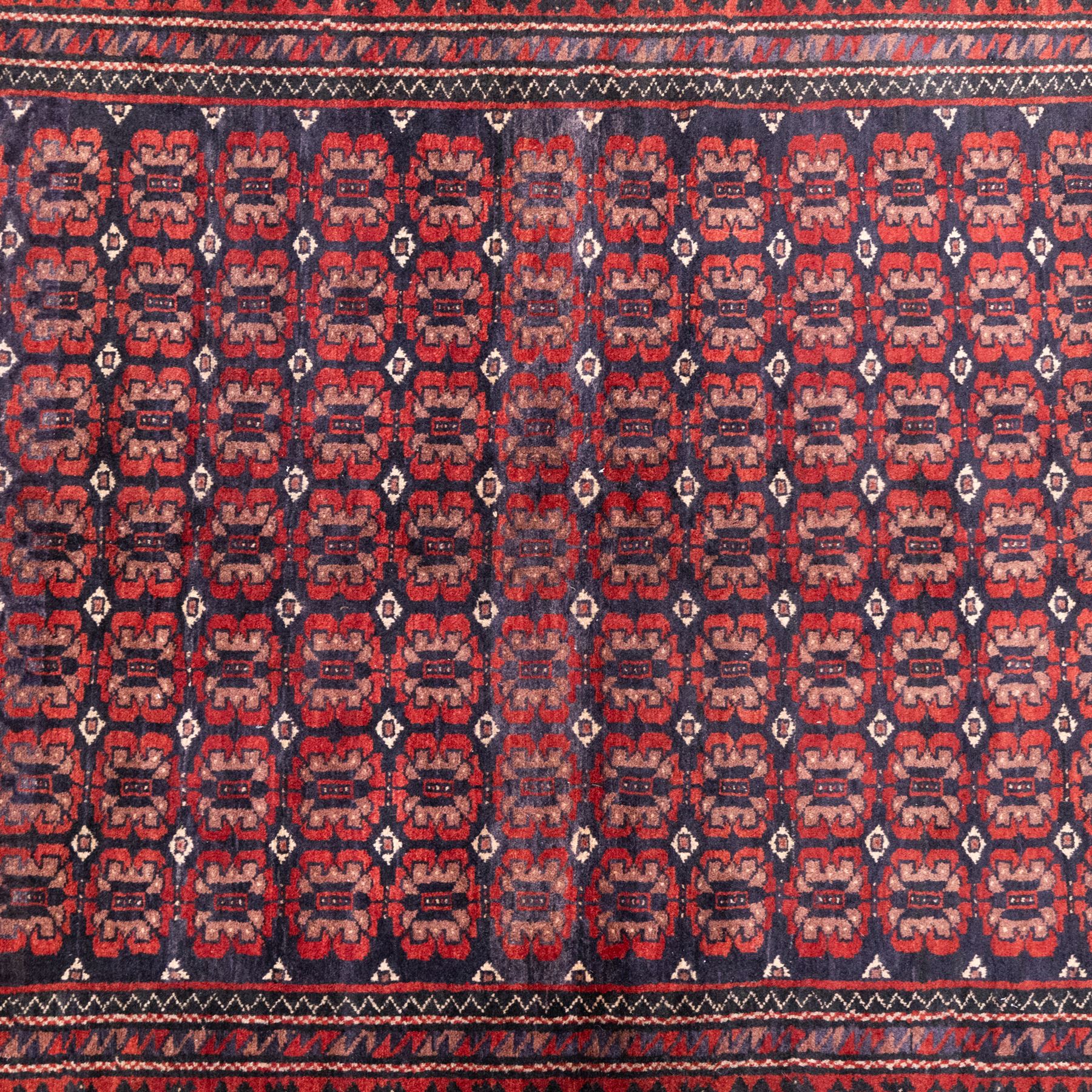 North East Persian Turkoman hand-knotted rug, indigo field densely decorated with an all-over repeating design of geometric gul motifs in shades of madder red, aubergine, and dark brown, highlighted with small ivory details, framed by multiple narrow guard borders and a main border with angular geometric motifs flanked by zig-zag borders, with cotton fringe ends 