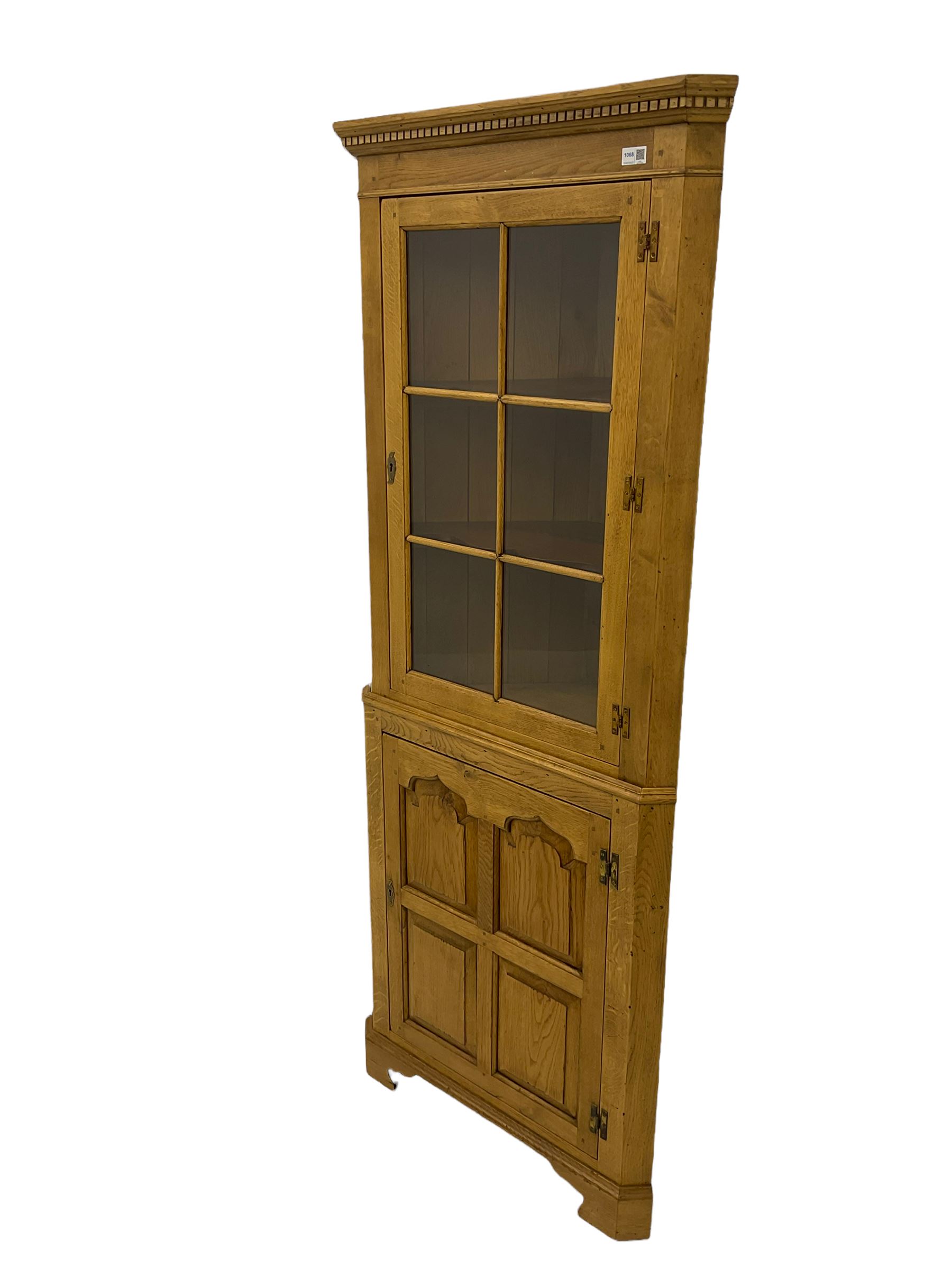 Traditional light oak corner cabinet, projecting cornice, dentil frieze, single glazed door above single fielded door