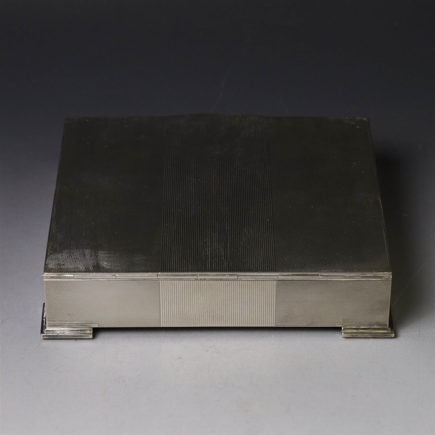 1960s silver mounted cigarette box, of rectangular form with engine turned decoration, upon four bracket feet, with presentation engraving to interior lid reading  'British Aircraft Corporation (Operating) Limited Commemorating the Queen's Award to Industry 1967, hallmarked James Geraghty, Birmingham 1965, with retailers mark for Asprey, W16.5cm, H4.5cm