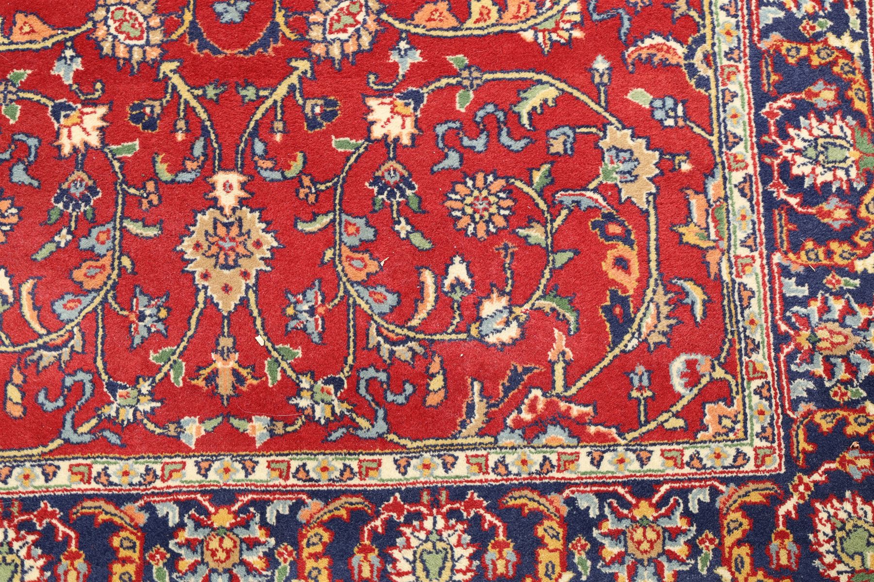 Persian Kashan crimson ground rug decorated with scrolling foliage, the indigo guard stripes with repeating stylised palmette motifs