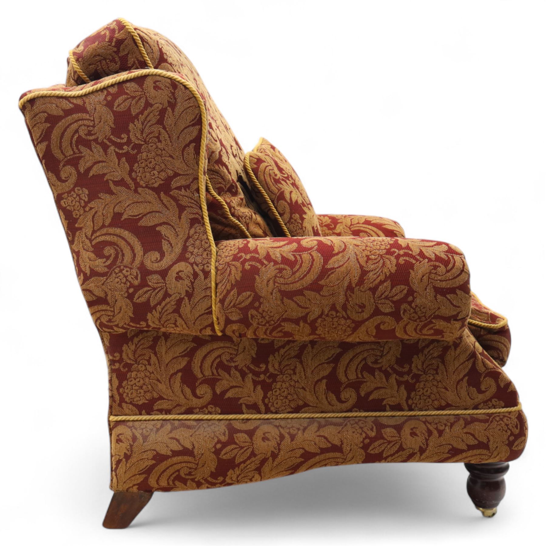 Duresta – pair of armchairs, upholstered in red and gold damask fabric with piped edges, scroll arms and loose feather-filled cushions, raised on turned wooden feet with brass castors