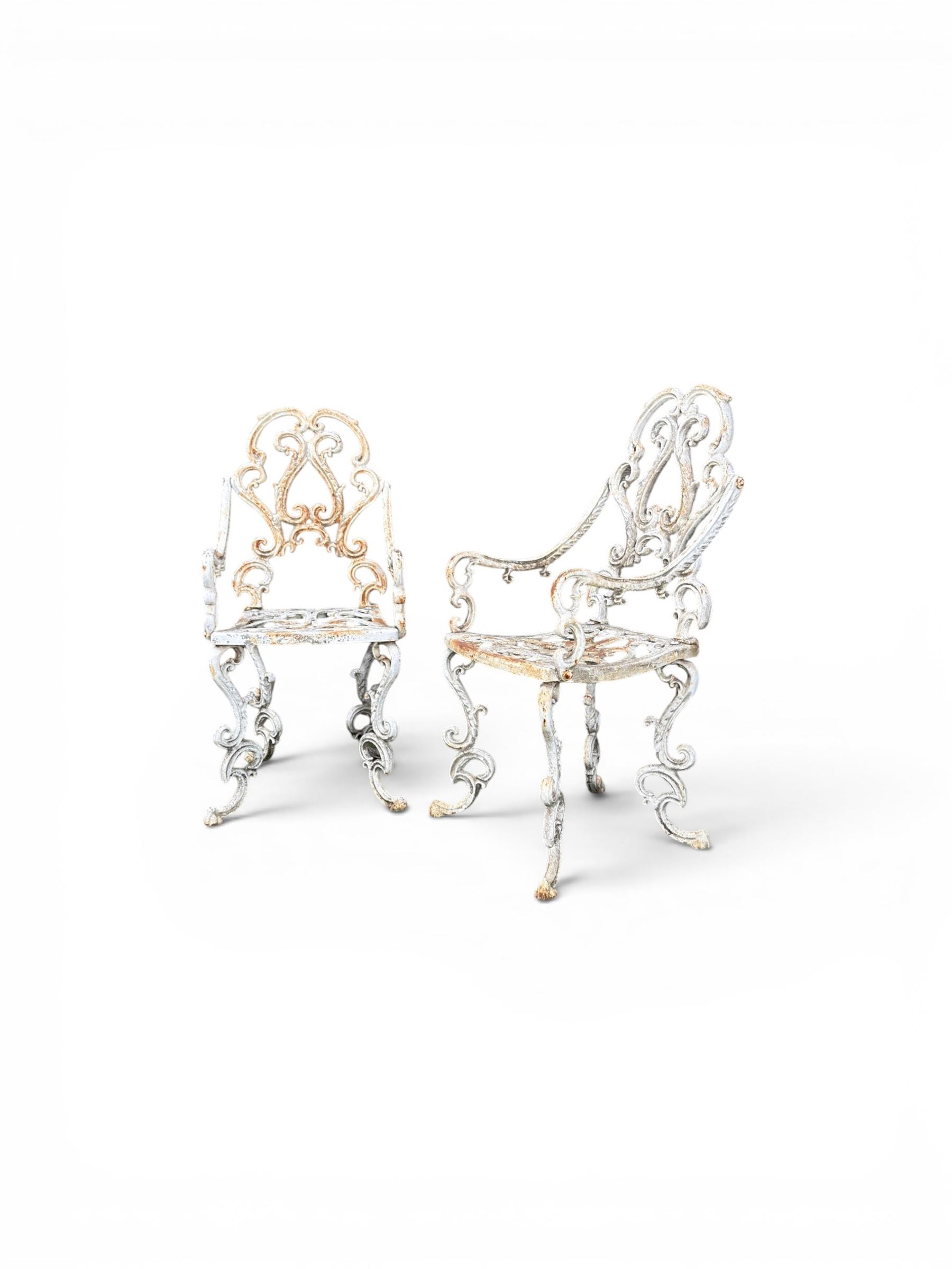 Pair of Victorian cast iron garden chairs, the ornate pierced back of scrolling foliate design, scrolling arm terminals over splayed supports formed of C and S-scrolls, in distressed white painted finish