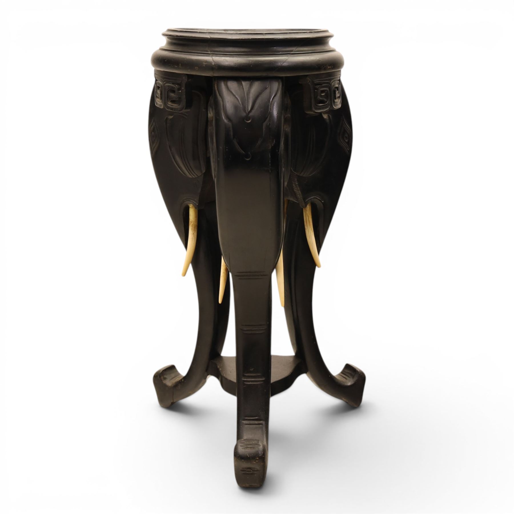 Oriental design black lacquered jardinière stand, circular moulded top with raised rim, the base formed as three elephant heads with carved ears and simulated tusks, on shaped supports with paw terminals