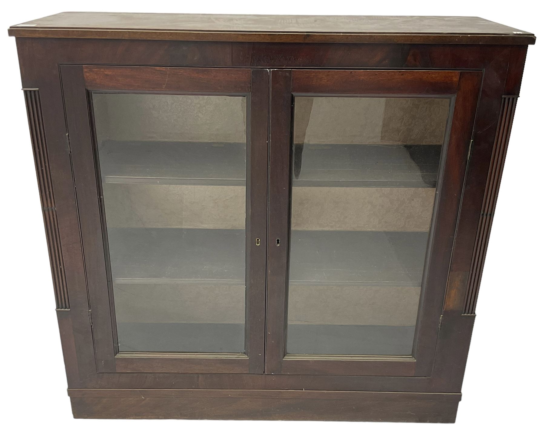 Edwardian mahogany enclosed bookcase, fitted with two glazed doors enclosing two shelves, flanked by reeded uprights, on skirted base