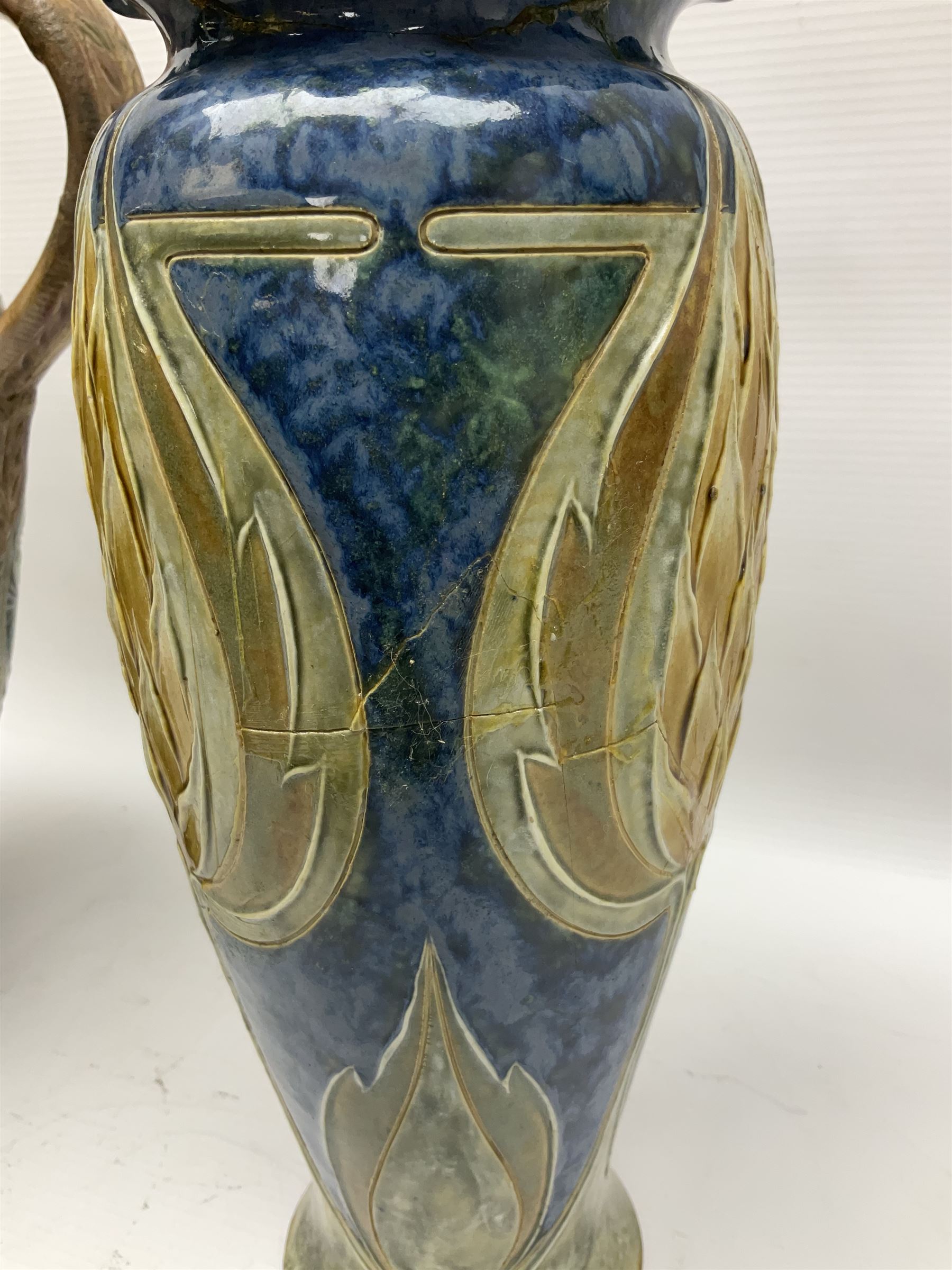 Early 20th century Royal Doulton stoneware vase, decorated with a stylized floral design below a wavy rim, monogrammed B.N, possibly for Bessie Newbery, H28cm, together with an early 20th century glazed jug, heavily carved throughout (2)