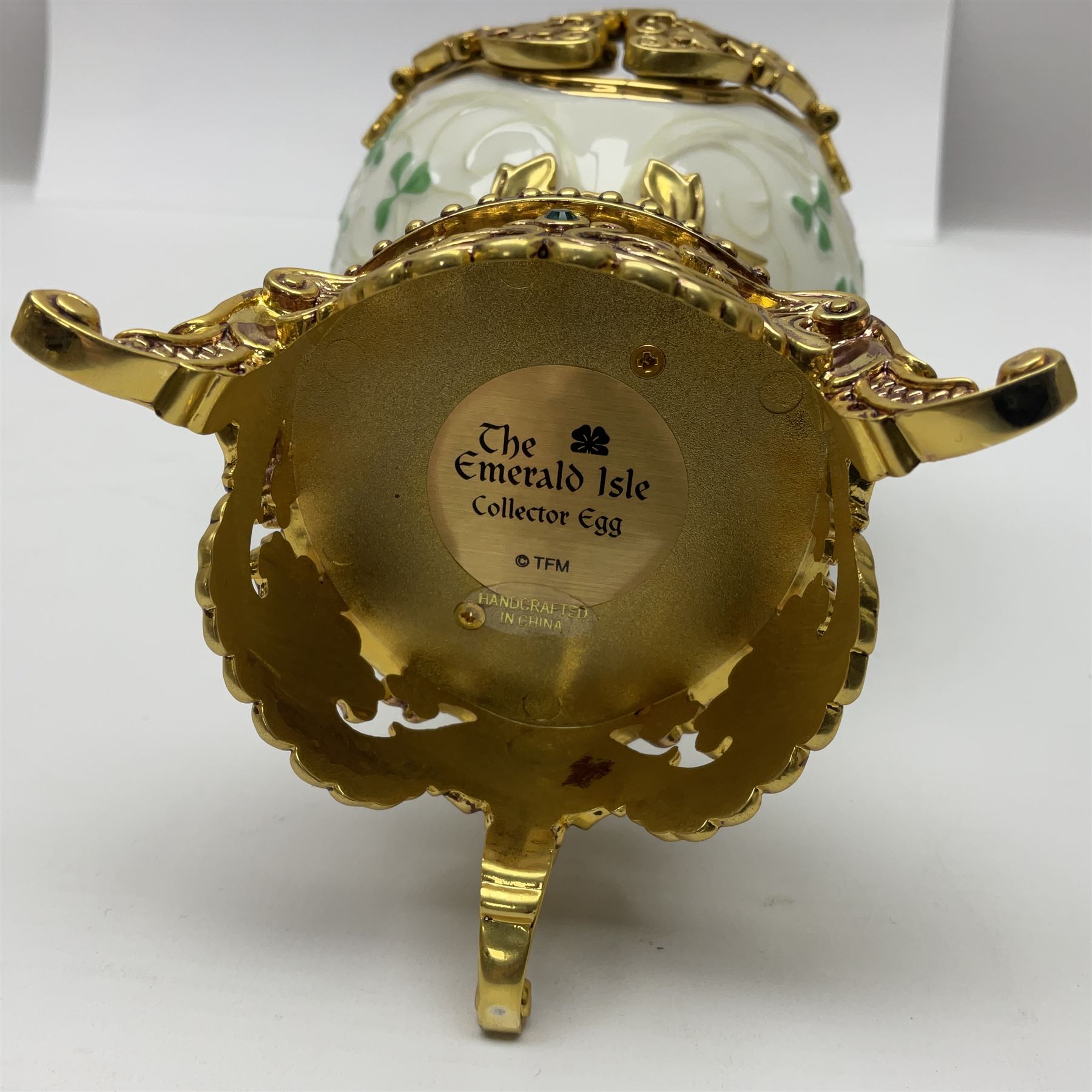 Franklin Mint The Emerald Isle Collector Egg, the egg decorated with embossed shamrocks upon a cream ground, with a gilded shamrock finial, accents and openwork door, opening to reveal a miniature landscape scene, upon three gilded feet set with green paste stones, with certificate of authenticity H23cm, 