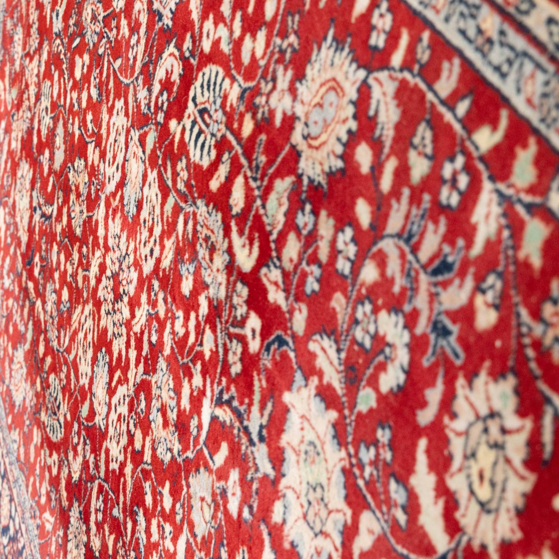 Persian crimson ground rug, interlacing floral stems linking ivory palmettes, rosettes and serrated leaves, within a navy floral border flanked by ivory patterned guards