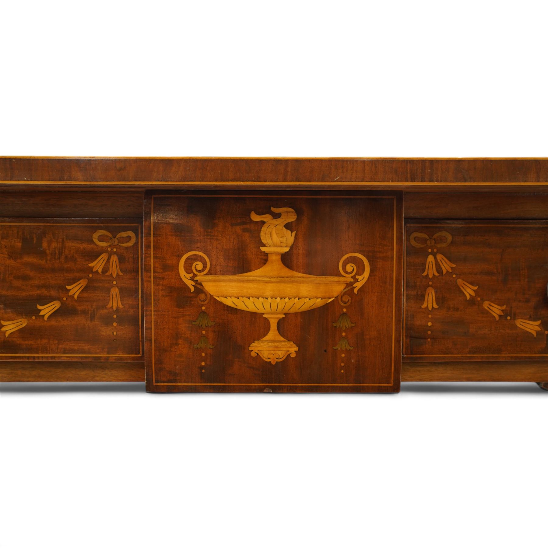 Edwardian Sheraton Revival inlaid plum pudding mahogany serpentine sideboard, rectangular top with raised gallery above bowed frieze drawer finely inlaid with central neoclassical urn motif, flanked by two drawers with swags and ribbon bows, above a cellarette drawer and cupboard, on square tapered supports with spade feet 