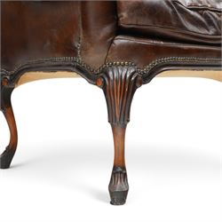 Pair of quality Queen Anne design mahogany framed wingback armchairs with matching footstools, the high sprung winged backs over rolled arms with studwork, raised on elegant reeded scroll carved cabriole supports, upholstered in deep chocolate brown leather (W82cm D75cm H112cm), the footstools with ovoid padded seat over studwork and moulded lower rail and cabriole supports (W65cm D42cm H48cm)