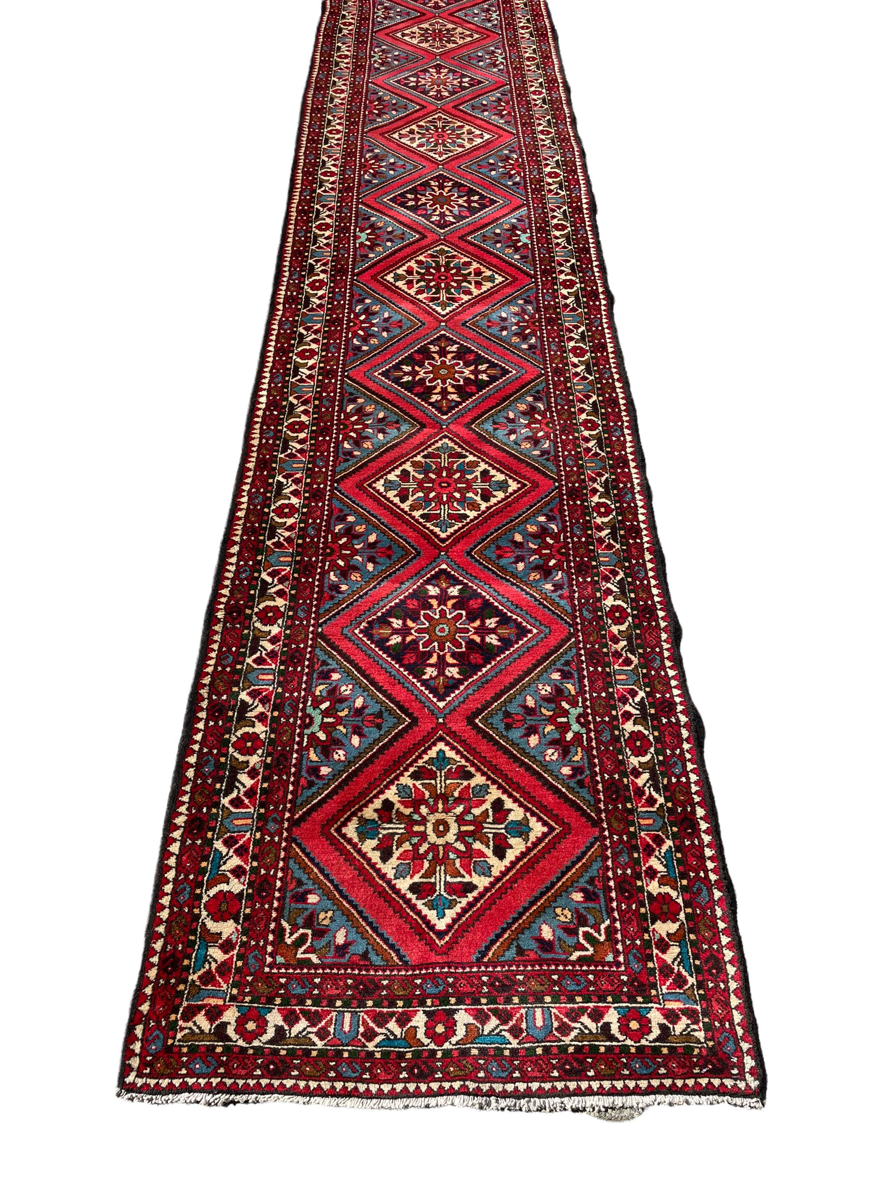 Persian Hamadan runner, red ground, decorated with eighteen lozenge medallions decorated with stylised floral motifs, three band border decorated with plant motifs and geometric patterns