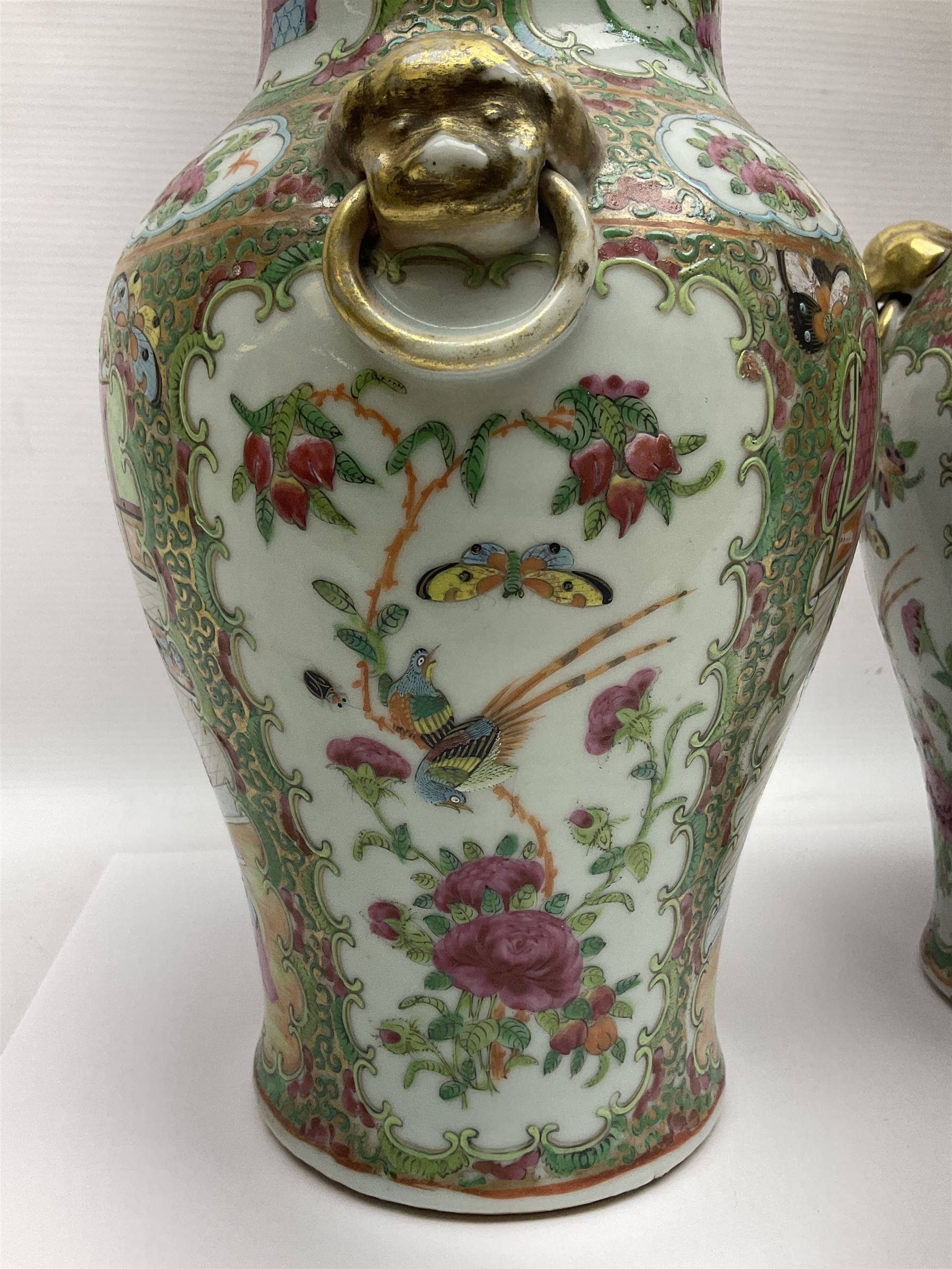 Pair of 19th century Chinese Famille Rose vases and covers, each of baluster form with twin gilt lion mask ring handles to shoulders, the flattened domed covers with gilt temple lion finials, each decorated with alternating reserves of bijin and attendants, and birds and butterflies amongst blossoming peonies, against a gilt ground profusely decorated with stylised scrolls, H32.5cm