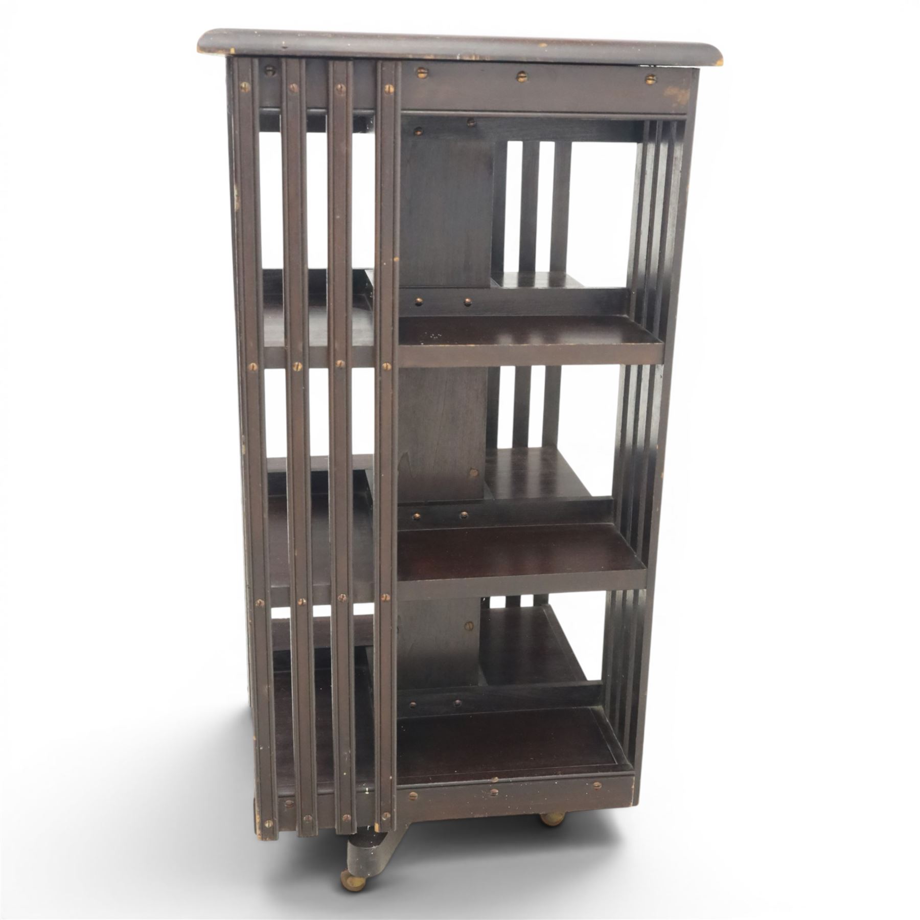20th century ebonised revolving bookcase, square top with chamfered edges, over a three tier with four sections per tier,  revolving base on castors 