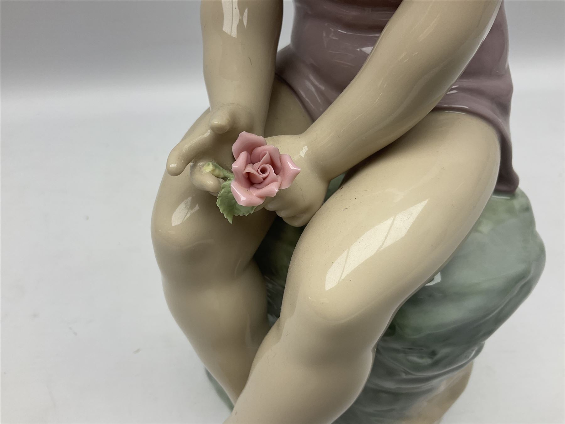 Large Nao figure modelled as a young girl seated upon a rock holding a rose, H30cm