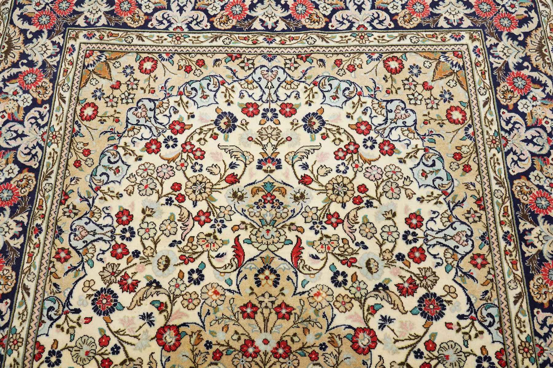 Central Persian Kashan hand-knotted carpet, ivory ground with a central floral medallion with an all-over design of scrolling vinery, palmettes, and flowering sprays i tones of madder red, cobalt, navy blue and sage green, with conforming spandrels, main border of deep indigo ground with repeating palmettes and stylized floral heads, flanked by narrow guard stripes, with cotton fringe ends, with cotton fringe ends 