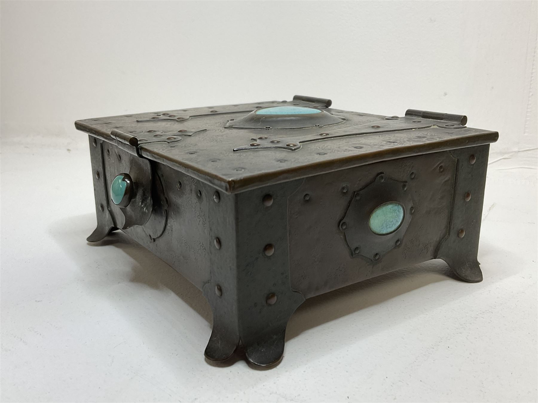Arts and Crafts copper box, the lid decorated with stylised riveted hinges and inset with Ruskin type ceramic turquoise heart-shaped cabochon, the mount etched M.B 1913, and further cabochon roundel to each side panel, including one inset to the clasp acting as the knob to the locking mechanism, marked RS Douglas 1913 beneath, W16.5cm H7cm D15cm