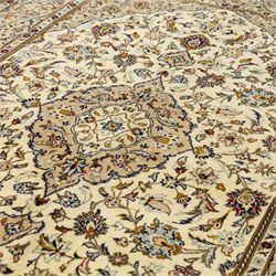 Central Persian Kashan hand-knotted rug, ivory ground, with a central shaped floral medallion with pendants, surrounded by scrolling foliate and floral motifs incorporating rosettes, palmettes and delicate vine work, enclosed by a beige border with repeating palmettes and meandering vines, flanked by narrow floral guard stripes, with cotton fringes