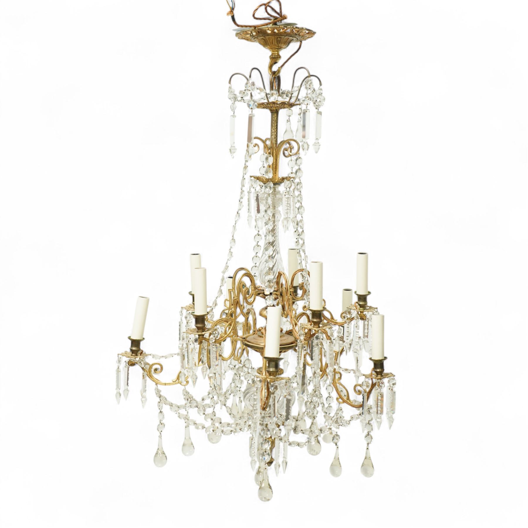 Late Victorian gilt bronze mounted crystal chandelier, ceiling rose above shaped top of trailing swags, glass crystal droplets, beneath rising curled branches and glass beads tapering down to five candle sconces, inside circular bezel fitted with drops and glass twist fluted stem, supported with an internal metal shaft above a rococo style stem holding double branches, and similar styled branches, with twelve branches fitted with candle holders and drip trays with crystal drops and cut crystal spears, the underside festooned with crystal glass swags and a bulbous fluted glass terminal and shaped finial with crystal glass swags attached to the branches, the base with pear shaped droplet graduating to the centre, wired for electricity 