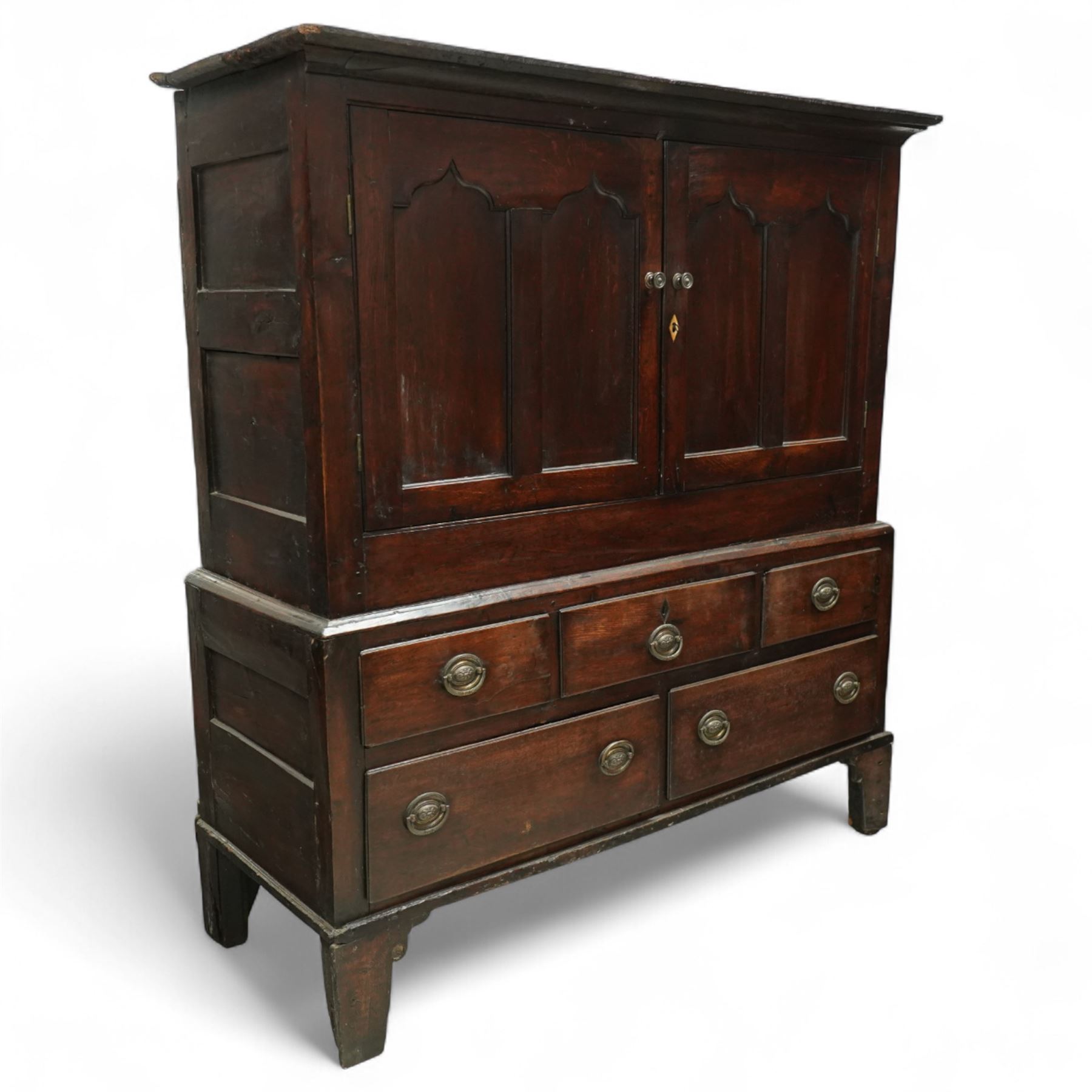 18th century oak dwarf press cupboard, the upper section with twin arched panel doors above three short and two long drawers, each with brass plate handles, shaped apron and stile feet, of compact country form