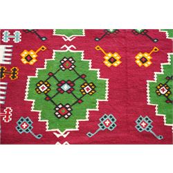 Persian Fars province crimson ground kilim rug, decorated with two rows of geometric emerald green motifs containing stylised plant designs, enclosed by an ivory and dark indigo guard band