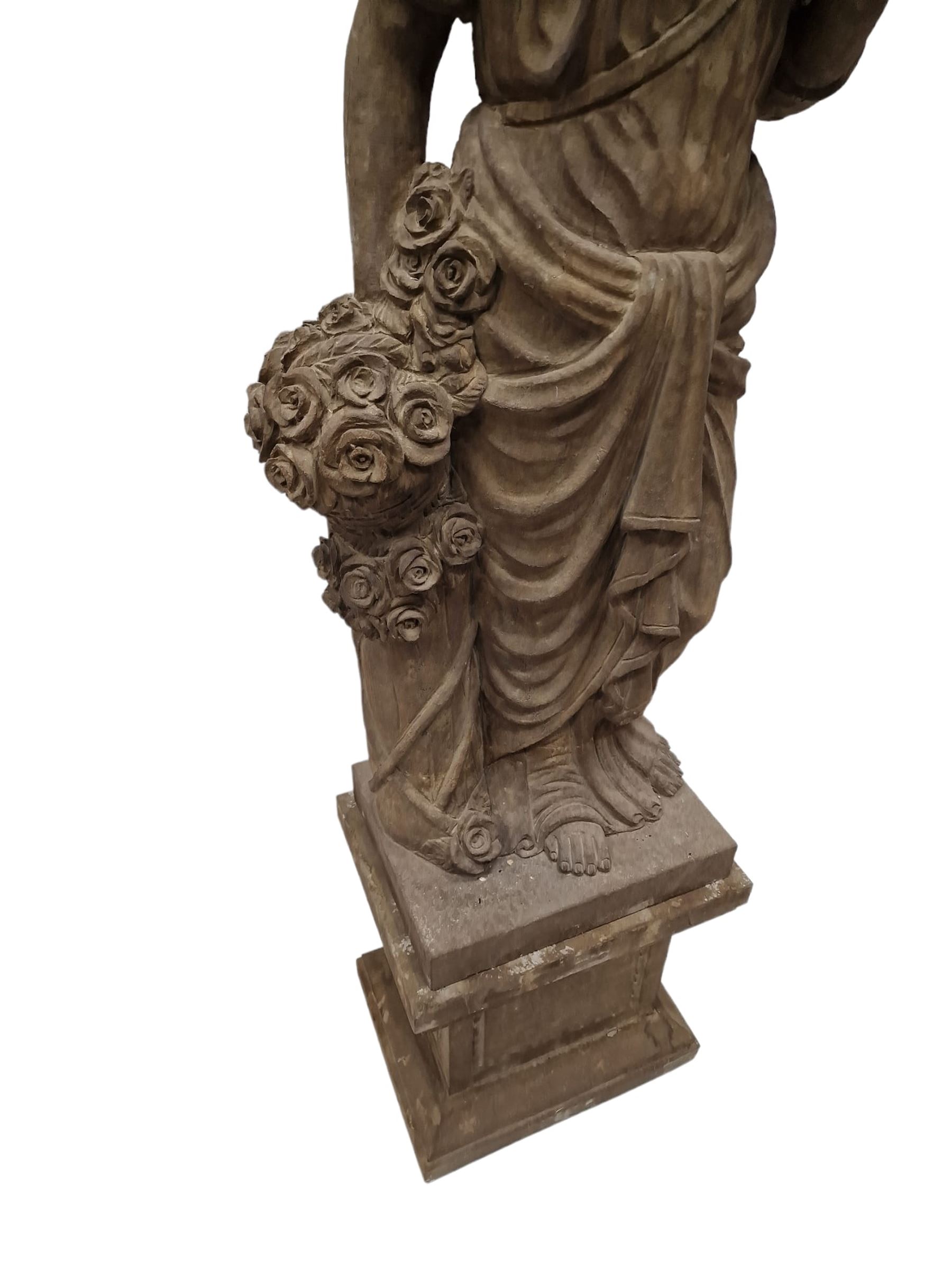 Hand carved stone Neoclassical figure of the Roman goddess Flora, her hair pinned with roses, draped in a toga, holding a basket of flowers in her right hand, raised on a stepped square plinth base 