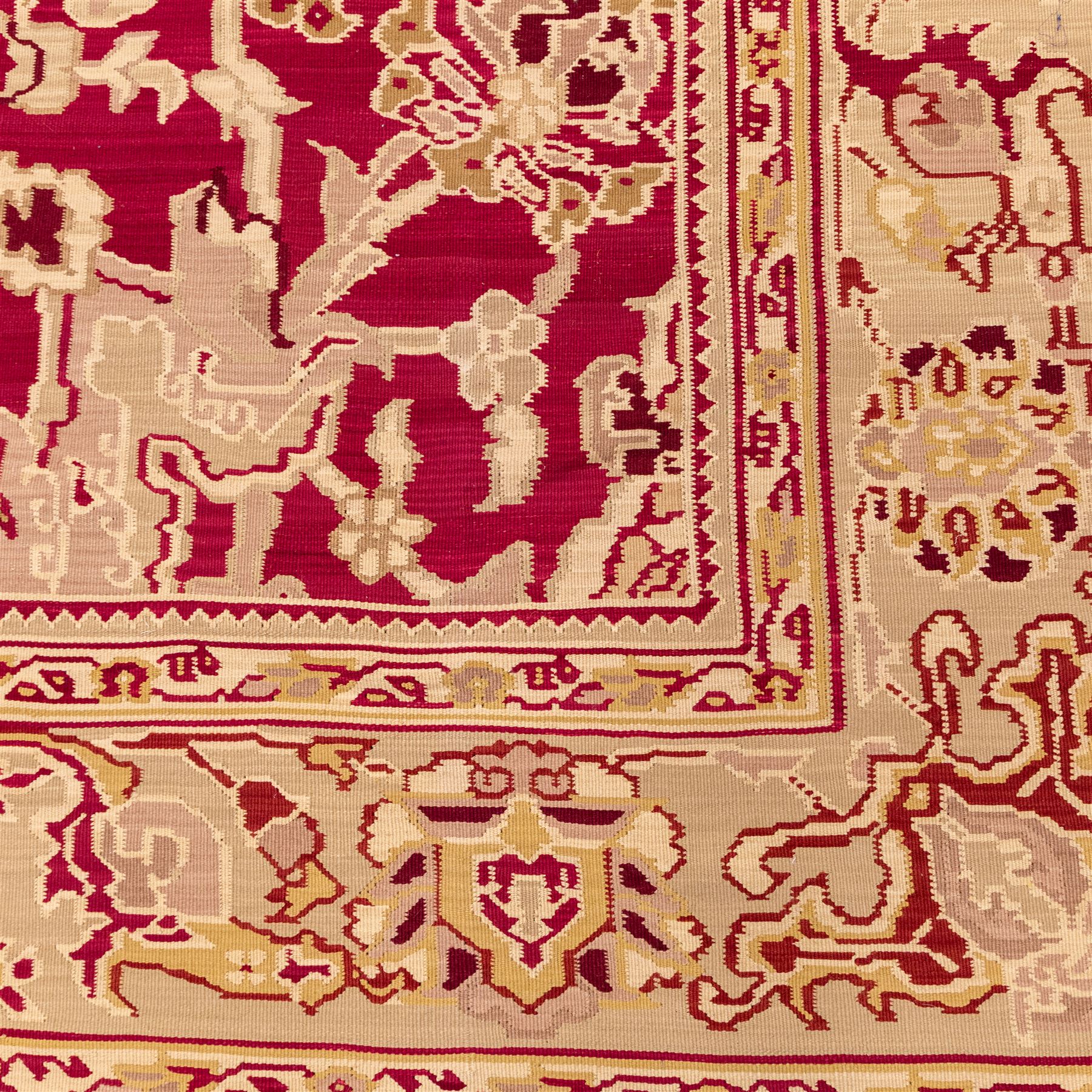 Large Persian Savonnerie-inspired style flatweave kilim, crimson field with central stylized palmette medallion with bold scrolling vinery and angular floral motifs between multiple guard stripes, rendered in tones of soft cream, pale sage, and muted terracotta, with fringe ends 