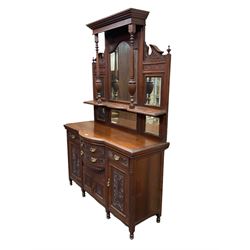 Edwardian walnut sideboard, projecting cornice supported by turned supports, the back fitted with three bevelled mirrors beneath fluted and flowerhead carved friezes, the lower section with four drawers and four panelled cupboard doors carved with foliate and urn designs, fluted uprights on turned feet