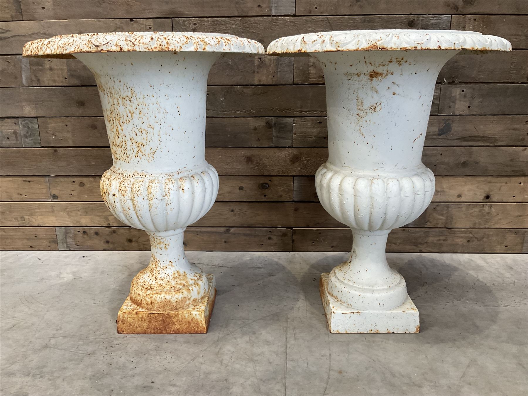 Pair of large Victorian design white painted cast iron campana shaped garden urns, egg and dart rim over a gadrooned underlobe, tapering column on square plinth base