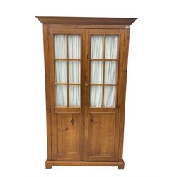 Rustic waxed pine double wardrobe, glazed doors with interior curtain, enclosing hanging rail, on bracket feet