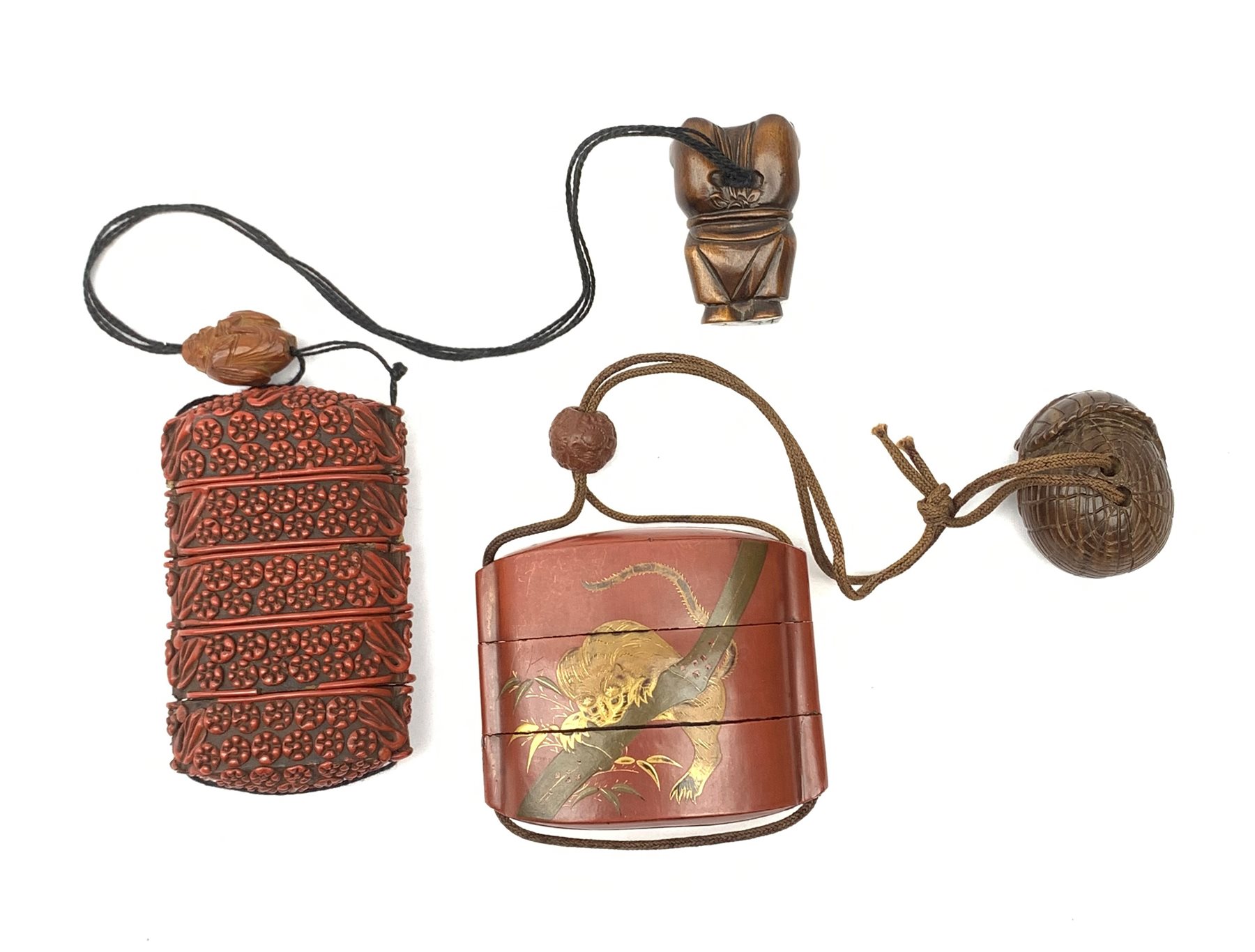 A Japanese cinnabar lacquer inro, of five sectional form, the whole with carved foliate detail, with wooden ojime, and carved hardwood Netsuke modelled as one of the Lucky Gods, Fukurokuju standing upon his hands, inro H8.5cm, together with a Japanese lacquer inro, of three sectional form, detailed with a tiger and bamboo branches, with ojime, and wooden netsuke modelled as a basket with animals within, inro H6cm.