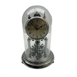 A 20th century German “Olympia” torsion suspension clock, with a silver effect base and four ball rotary pendulum, silver effect dial with Arabic numerals and minute track, with steel baton hands, plain silvered bezel under an acrylic dome.
No Key. 

