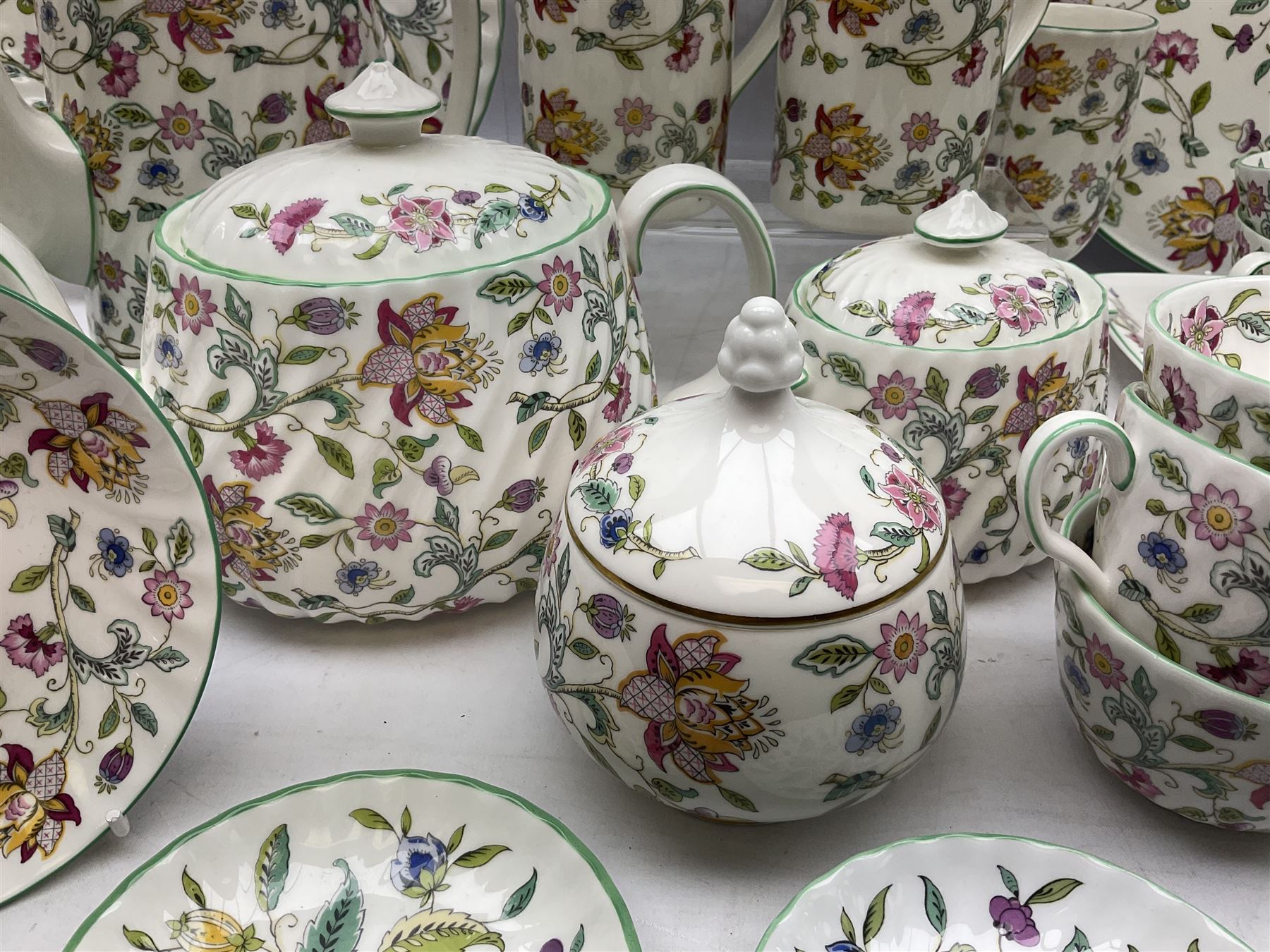 Minton Haddon Hall pattern tea and dinner wares, including basket dish, two covered tureens, six dinner plates, eight dessert plates, twelve tea plates, six soup bowls, six cereal bowls, teapot, coffee pot, milk jug, covered sucrier twelve tea cups and saucers, six mugs, footed bon bon dish, pair of candlestick holders, cake knife and slice etc (81)